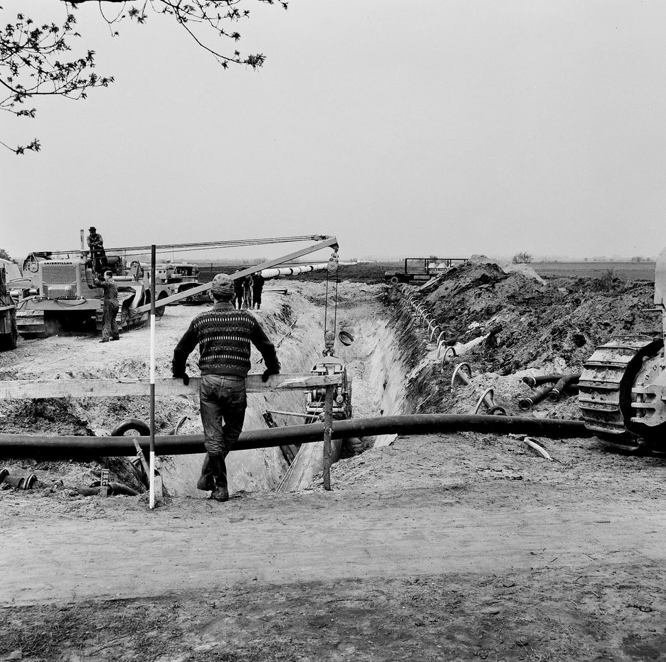 A local looks over the installation of pipes at the NAM gas fields near Groningen, c.1964.